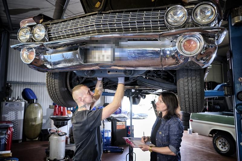 Maja und ein Mechaniker prüfen gemeinsam die Unterseite eines Oldtimers auf der Hebebühne