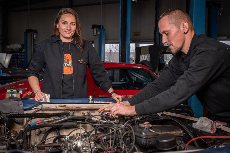 Maja und ein Mechaniker besprechen gemeinsam einen geöffneten Motor